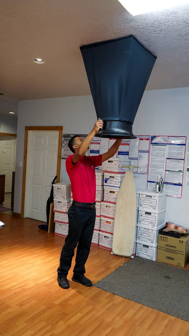 Technician holding a flow hood up to a ceiling supply register to measure airflow